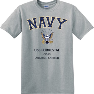 Könnte beinhalten: Ein graues T-Shirt mit einer marineblauen Grafik des Wortes "NAVY" mit einem goldenen Adler- und Ankeremblem. Der Text "USS FORRESTAL CV-59 AIRCRAFT CARRIER" ist unter dem Emblem gedruckt.