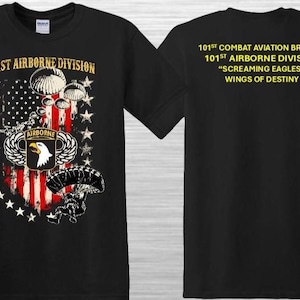 May include: Black t-shirt featuring a design with the text "101st Airborne Division" and an American flag motif. The design includes parachutes, stars, and an eagle emblem. The back of the shirt displays additional text: "101st Combat Aviation Brigade" and "Wings of Destiny."