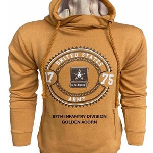 Può includere: Felpa con cappuccio color senape con cappuccio con coulisse e una grande grafica sul davanti. La grafica presenta un design circolare con le parole "UNITED STATES ARMY" e una stella. È visibile anche il testo "87TH INFANTRY DIVISION GOLDEN ACORN".