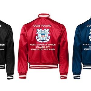 Puede incluir: Tres chaquetas bomber de sat&eacute;n en negro, rojo y azul marino. Cada chaqueta presenta las palabras "COAST GUARD" sobre un emblema de la Guardia Costera y el texto "COAST GUARD AIR STATION ATLANTIC CITY ATLANTIC CITY-NEW JERSEY".