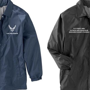 May include: Two jackets, one navy blue and one black, with a white embroidered logo and text that reads "FLY-FIGHT WIN PATRICK AIR FORCE BASE BREVARD COUNTY FLORIDA US AIR FORCE".