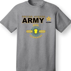 Può includere: Una maglietta grigia con il testo "UNITED STATES ARMY 87th INFANTRY DIVISION GOLDEN ACORN" e una stella gialla con il testo "U.S. ARMY".