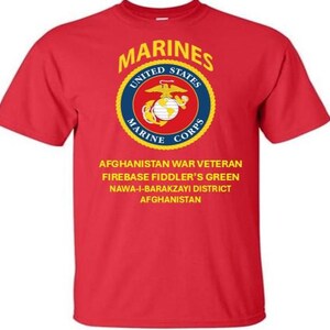 Könnte beinhalten: Rotes T-Shirt mit dem Emblem der US Marines in einem kreisförmigen Design mit den Worten "MARINES", "UNITED STATES MARINE CORPS". Darunter steht "AFGHANISTAN WAR VETERAN FIREBASE FIDDLER'S GREEN NAWA-I-BARAKZAYI DISTRICT AFGHANISTAN."