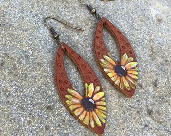 May include: A pair of brown leather earrings featuring a sunflower design. The earrings are painted with yellow, orange and green paint.