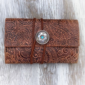 May include: A brown leather wallet with a paisley pattern and a silver concho with a turquoise stone.
