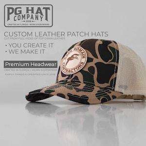 May include: A camouflage pattern hat with a leather patch that reads "Cape Romain Contractors." The hat has a mesh back and a curved brim. The text "PG Hat Company" is visible in the upper left corner.