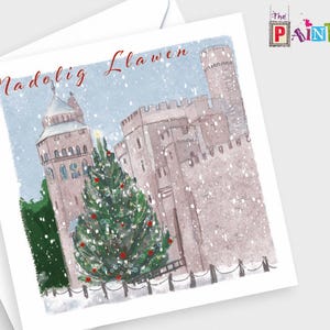 May include: A Christmas card with a watercolour illustration of a castle in a snowy scene. A decorated Christmas tree is in front of the castle. The words "Nadolig Llawen" are written in red script. The Paintbox logo is in the upper right corner.