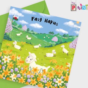 May include: A greeting card with a green envelope. The card features a colorful illustration of sheep in a field of daffodils, with a Welsh flag and the words "Pasg Hapus". The sky is blue with fluffy clouds.