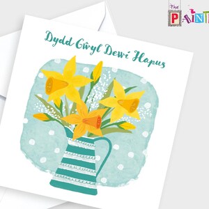 May include: Greeting card with a watercolor illustration of yellow daffodils in a teal and white striped pitcher. The card has the text "Dydd Gwyl Dewi Hapus" in teal script. The card is on a white background with a white envelope.