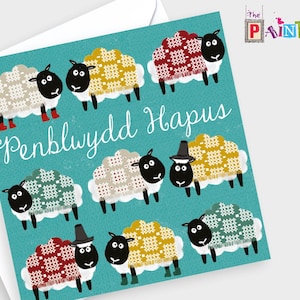 May include: A greeting card with a blue background and the text "Penblwydd Hapus" which means "Happy Birthday" in Welsh. The card features a pattern of black and white sheep wearing colorful knitted sweaters.