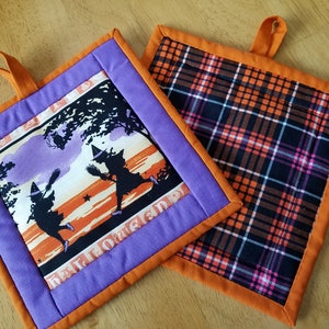 May include: Two Halloween-themed pot holders. One is purple with an orange border and features a vintage illustration of two witches flying with brooms. The other is orange with a black and white plaid pattern.