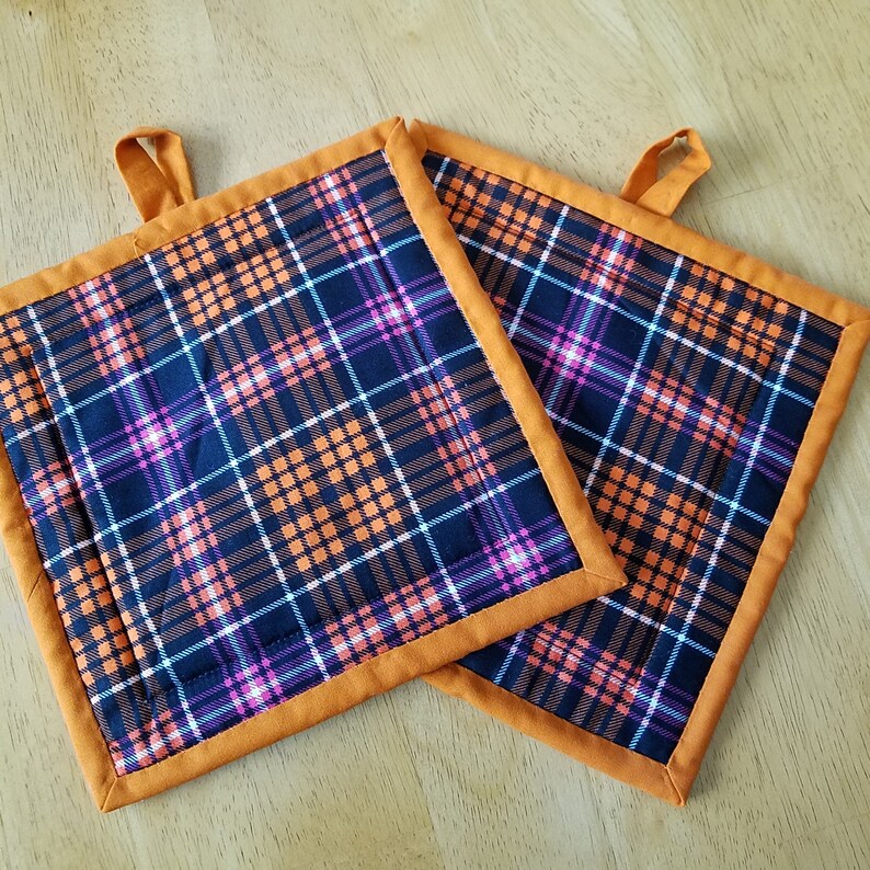 May include: Two orange and black plaid pot holders with orange trim. The pot holders have a loop for hanging.