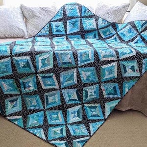 May include: A quilt featuring a repeating pattern of blue and teal fabric squares in various shades and textures. The squares are separated by a black fabric with small white polka dots, creating a diamond-like grid effect across the entire surface.