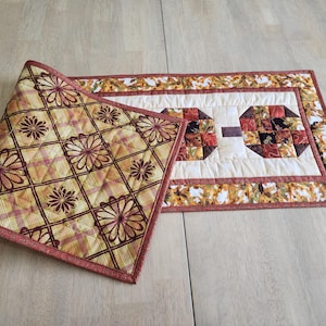 以下が含まれることがあります： キルト加工されたテーブルランナーと、お揃いのプレースマット。 ランナーは幾何学模様の中央のデザインと、秋の葉のボーダーが特徴です。 プレースマットは、黄色、赤、茶色の花柄とチェック柄です。