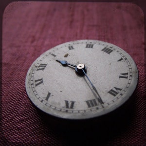 Peut inclure: Un cadran d'horloge de style vintage avec des chiffres romains et des aiguilles noires. Le cadran de l'horloge est blanc et a un aspect usé et vieilli. L'horloge est réglée sur 12h00.