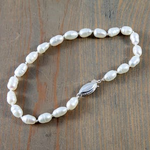 May include: A white pearl bracelet with a silver clasp. The pearls are oval shaped and strung together on a silver chain.