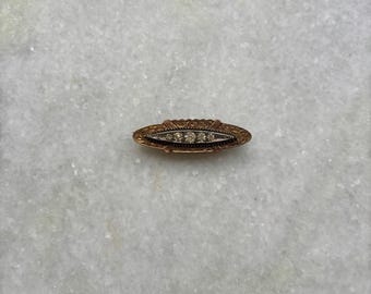 May include: A gold oval-shaped brooch with a row of five clear diamonds set in the center.