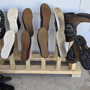 May include: A wooden shoe rack holding various shoes and boots. The rack is made of light-colored wood and has multiple slots to hold the footwear. The shoes and boots are of different styles and colors, including black, brown, and white.