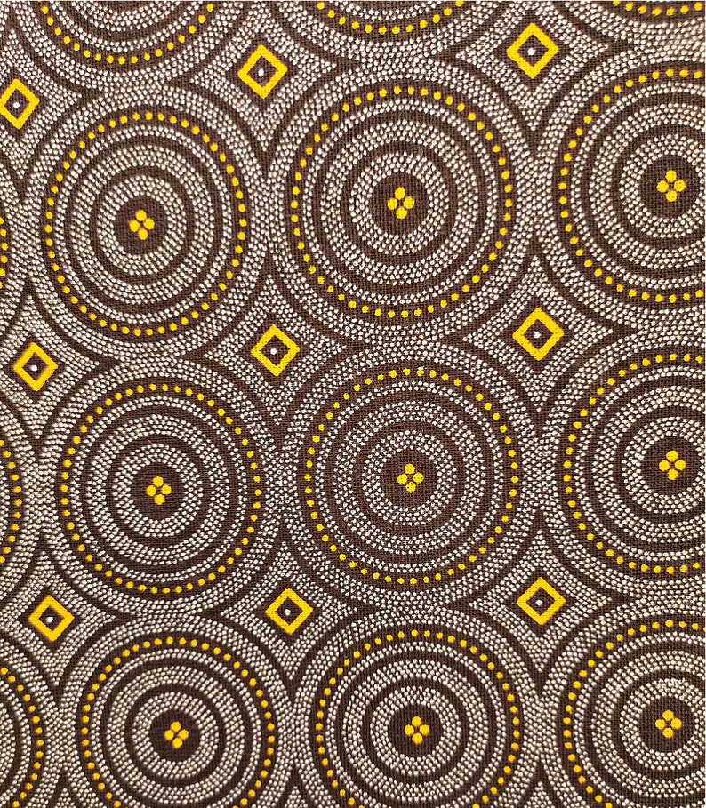 May include: A brown fabric with a repeating pattern of white and yellow circles. The circles are made up of small white dots and have a yellow outline. There are also small yellow diamonds scattered throughout the fabric.