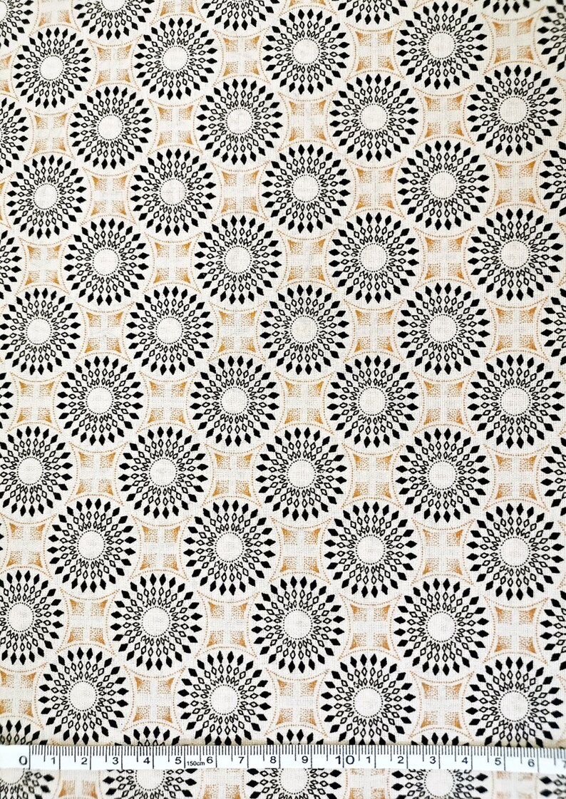 Puede incluir: Una tela beige con un patr&oacute;n repetitivo de c&iacute;rculos negros y dorados. Los c&iacute;rculos est&aacute;n formados por diamantes negros m&aacute;s peque&ntilde;os y est&aacute;n rodeados por un anillo dorado.