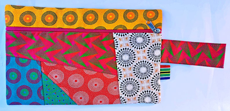 Pu&ograve; includere: Una pochette con cerniera colorata con un design patchwork che presenta motivi geometrici in tonalit&agrave; di rosso, giallo, blu, verde e bianco. La pochette ha una chiusura a zip e una tracolla rimovibile.