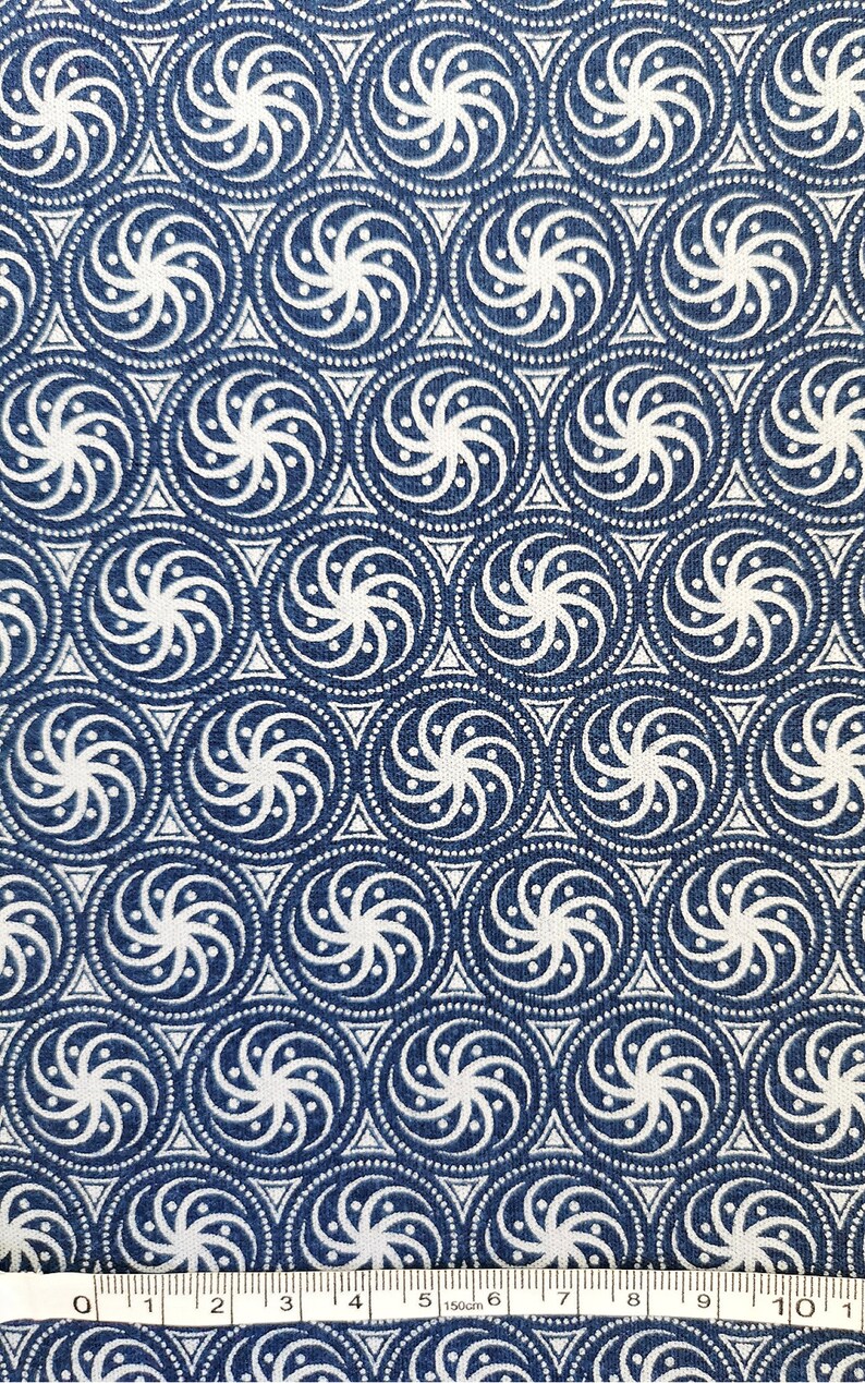 May include: A blue fabric with a white repeating pattern of swirling circles. The fabric is measured with a ruler in inches.