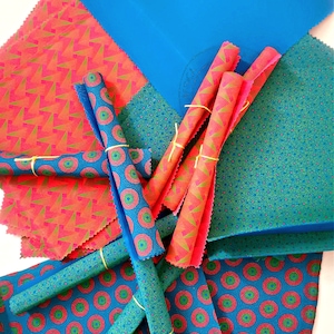 May include: A set of colourful reusable food wraps in blue, green and red patterns. The wraps are rolled up and tied with string.