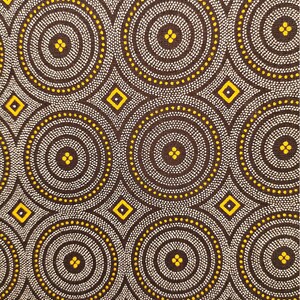 May include: Brown fabric with a repeating pattern of white and yellow circles and diamonds. The fabric is measured with a ruler in inches.