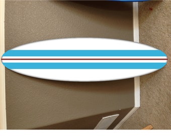 May include: A white surfboard with two blue stripes and a brown stripe. The surfboard is hanging on a wall.