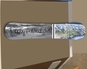 Może przedstawiać: Czarno-białe zdjęcie śnieżnego krajobrazu górskiego z nadrukowanym na snowboardzie tekstem "Tamarack, Idaho". Prawa strona snowboardu przedstawia kolorową mapę ośrodka narciarskiego.