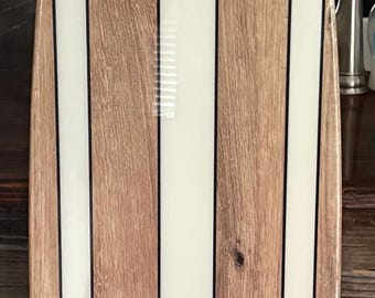 May include: A wooden surfboard with a unique design. The board features alternating vertical stripes of light wood and white resin, separated by thin black lines. The surfboard is approximately 152 cm long.