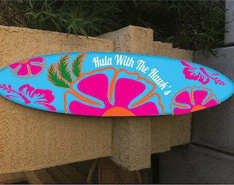 May include: A blue surfboard with a floral design and the text "Hula With The Hawk's" in white.