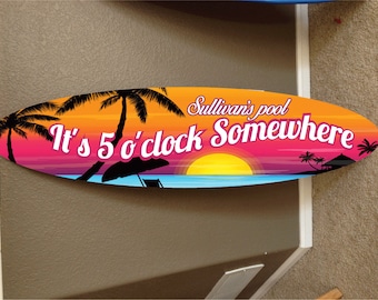 May include: A colorful oval-shaped sign with a sunset scene and palm trees. The text reads "Sullivan's pool It's 5 o'clock Somewhere".