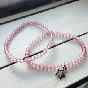 May include: Two pink beaded bracelets with a silver star charm. The bracelets are made of small, round beads and are stacked on top of each other.