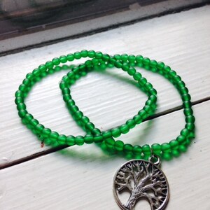 May include: A green beaded necklace with a silver tree of life pendant.