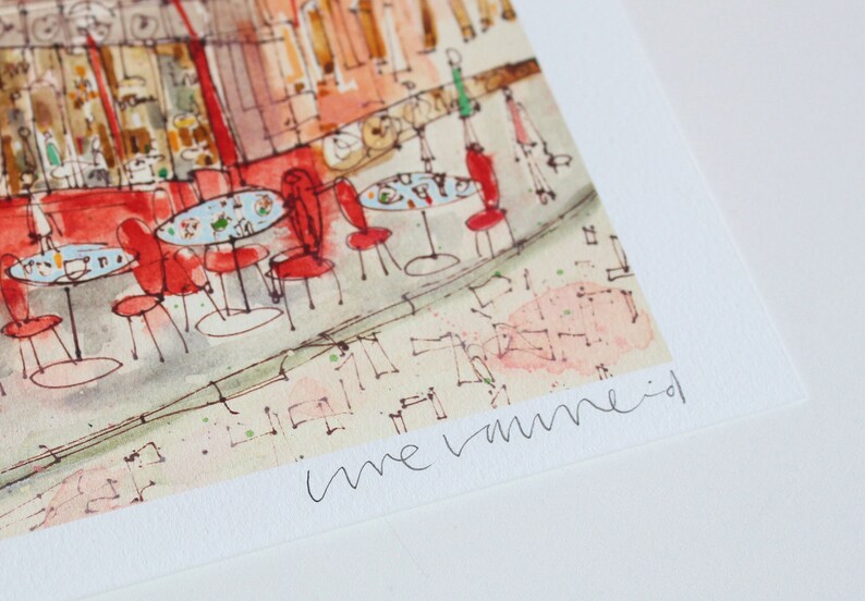 May include: Watercolor print of a cafe scene with red chairs and tables. The artwork depicts a street view with a cafe, featuring small round tables and chairs. The artist's signature is visible in the bottom right corner.