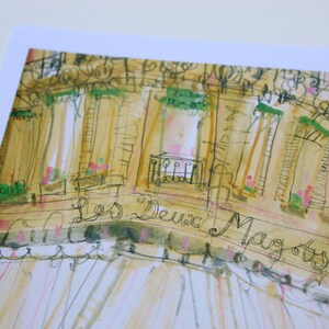 May include: Watercolor illustration of a building facade with the text "Les Deux Magots". The artwork features a warm color palette with beige, green, and pink accents, capturing a Parisian cafe scene.