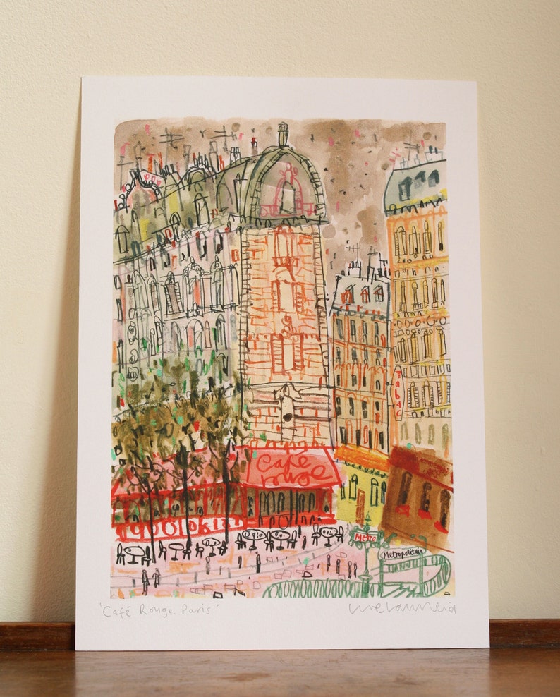 May include: A watercolor painting of a Parisian street scene with a cafe called "Cafe Rouge" and the text "Metro" and "M&eacute;tropolitain". The buildings are drawn in a whimsical style with a mix of orange, yellow, and brown colors.