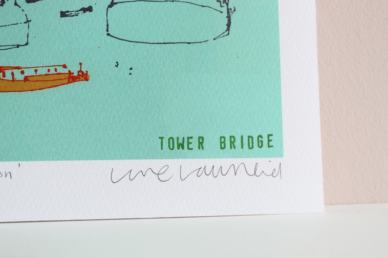 May include: A green and white print with a black and white illustration of Tower Bridge. The print is signed "une laumier" and titled "Tower Bridge".