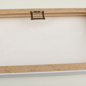 May include: A white canvas with a brown wooden frame and a metal hanging hook. The canvas is blank and ready for painting.
