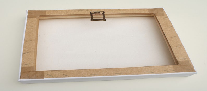 May include: A white canvas with a brown wooden frame and a metal hanging hook. The canvas is blank and ready for painting.