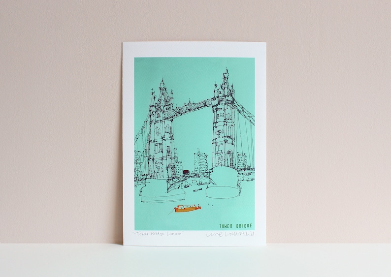 May include: A black and white line drawing of Tower Bridge in London, England. The bridge is drawn on a turquoise background. The text "Tower Bridge" and "Live, Love, London" are written below the bridge.