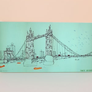 May include: A black and white line drawing of the Tower Bridge in London, England. The bridge is drawn on a light blue background with a flock of birds flying overhead. The text "TOWER BRIDGE" is printed in green at the bottom right corner of the image.