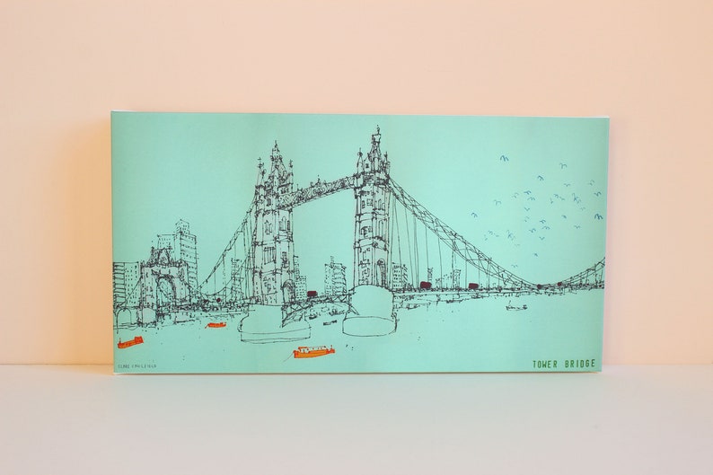 May include: A black and white line drawing of the Tower Bridge in London, England. The bridge is drawn on a light blue background with a flock of birds flying overhead. The text "TOWER BRIDGE" is printed in green at the bottom right corner of the image.