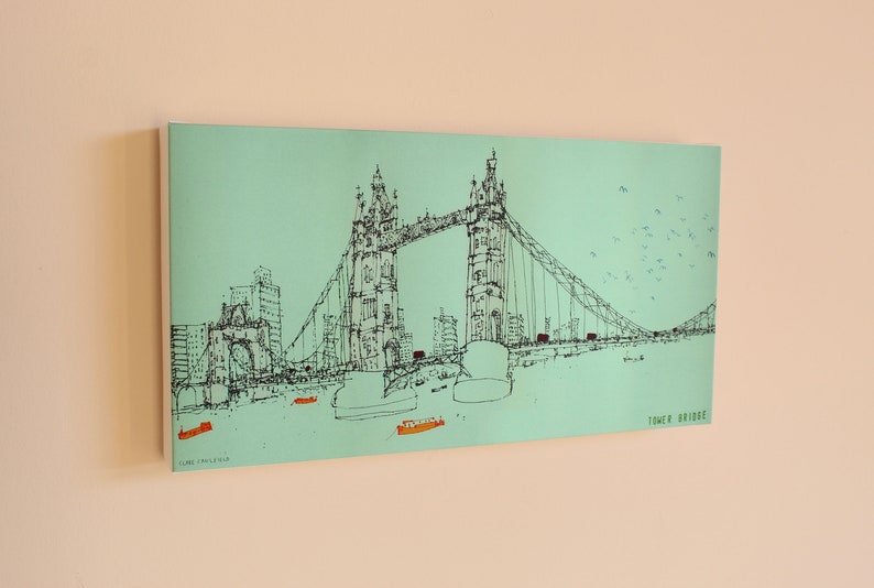 May include: A black and white line drawing of Tower Bridge in London, England. The bridge is drawn on a light blue background with small boats and birds in the sky. The text "TOWER BRIDGE" is in the bottom right corner.