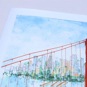 May include: A watercolor illustration of the Golden Gate Bridge in vibrant red, featuring thin suspension cables and a detailed city skyline in the background with blue water and small boats, all set against a light blue sky on white paper.