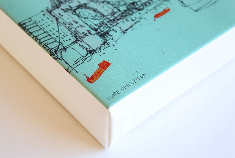 May include: A close-up of a turquoise canvas print with a black and white illustration of a city skyline. The print is framed with a white border and the artist's name, "CLARE CAULFIELD", is printed in black text on the bottom right corner.