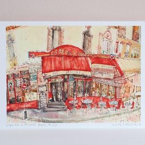 May include: Watercolor print of the Cafe des 2 Moulins in Paris, featuring a red awning and outdoor seating. The artwork depicts a street scene with buildings and the cafe's name visible. The print is numbered 15/150.