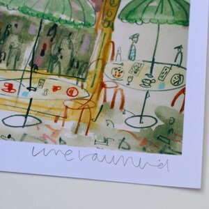 May include: Watercolor print of a cafe scene with tables, chairs, and green umbrellas. The artwork features red and blue accents, with the word "unerauniel" in the lower right corner. The style is reminiscent of a European cafe.
