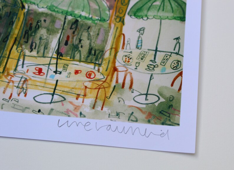 May include: Watercolor print of a cafe scene with tables, chairs, and green umbrellas. The artwork features red and blue accents, with the word "unerauniel" in the lower right corner. The style is reminiscent of a European cafe.